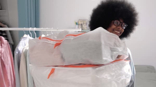 Une jeune femme qui sourit en portant une paire de boîtes-tiroirs blanches PÄRKLA avec des détails orange à côté d'un portant.