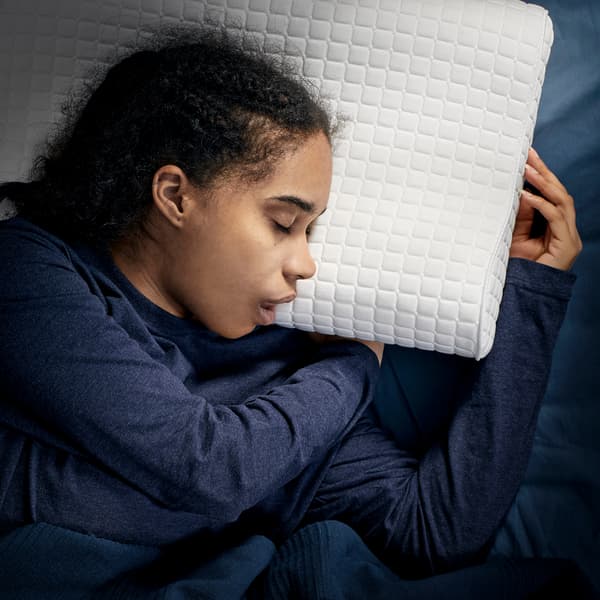 Une jeune fille couchée sur le côté dort profondément sur un oreiller ergonomique IKEA ROSENSKÄRM.