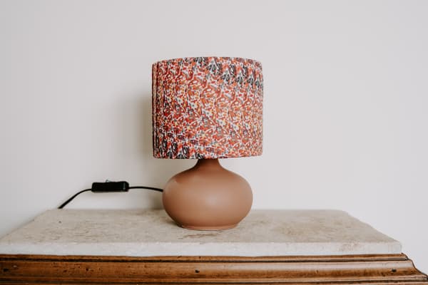 Une lampe de chevet avec un pied marron et un abat-jour à motifs rouge.
