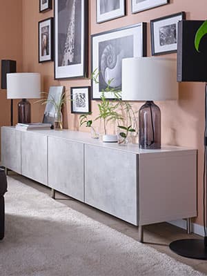 Une lampe de table posé sur une solution de rangement BESTA avec des portes effet marbre grise KALLVIKEN. Des cadres noires remplissent le mur de décoration.