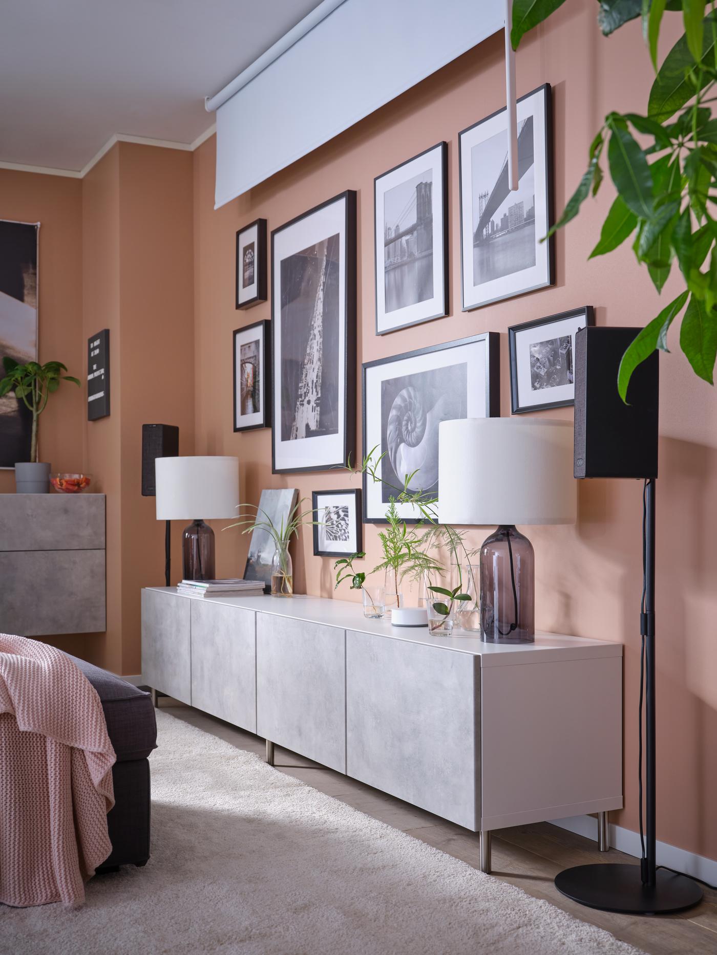 Une lampe de table posé sur une solution de rangement BESTA avec des porte effet marbre grise KALLVIKEN. Des cadres noires remplissent le mur de décoration.