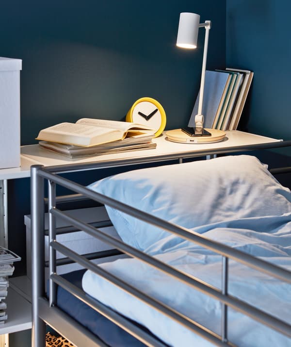 Une lampe de travail RIGGAD éclairant un coin à dormir et chargeant un smartphone.