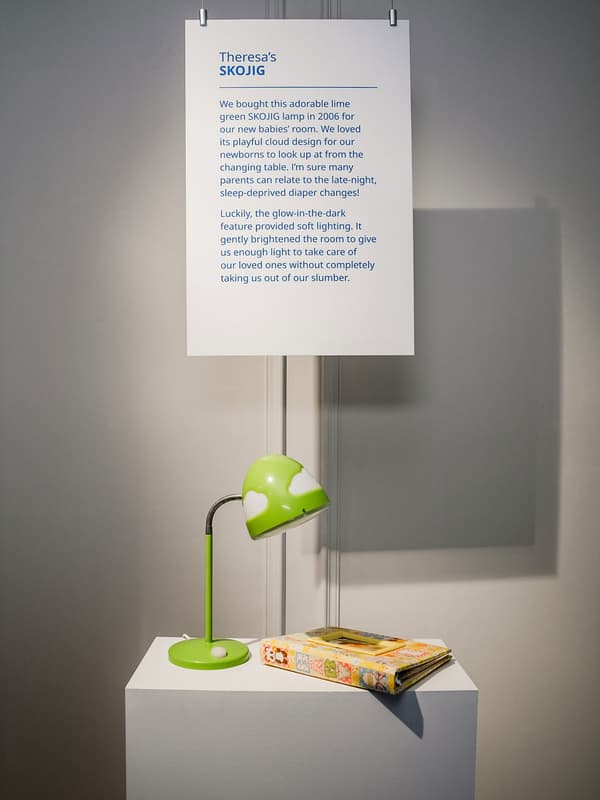 Une lampe SKOJIG verte pour bébés et enfants est en présentation à côté d’un album photo.