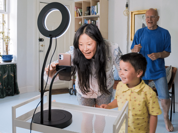 Une mère et son enfant installent un anneau lumineux avec support à téléphone LÅNESPELARE pour enregistrer une vidéo. Le père danse derrière eux.