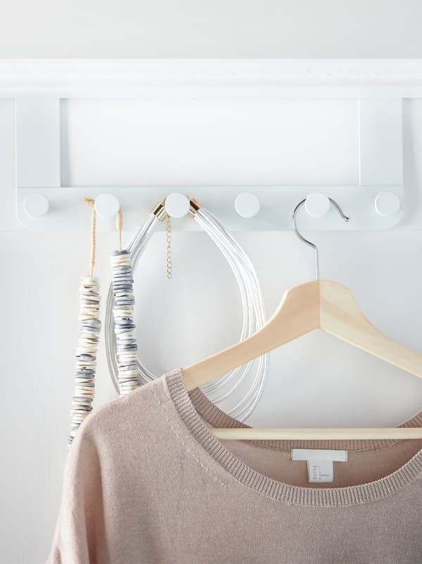 Une patère ENUDDEN avec boutons installée à l’arrière d’une porte, des accessoires et un haut suspendu à un cintre.