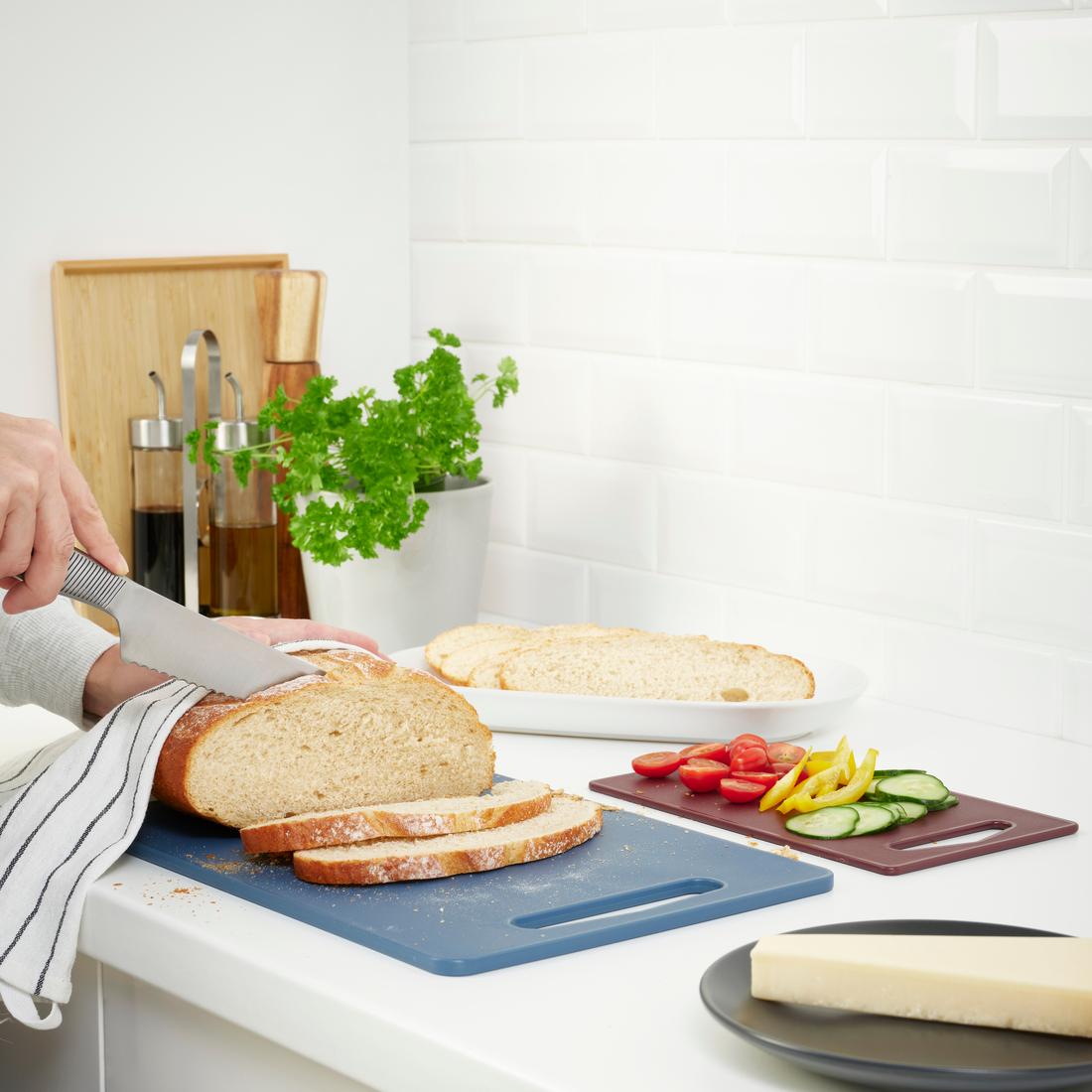 Une personne coupe du pain sur une planche à découper bleue.