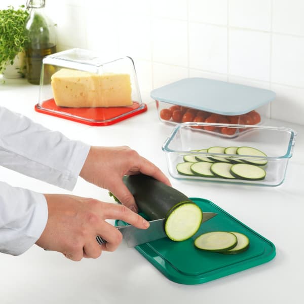 Une personne découpe une courgette sur une planche à découper verte