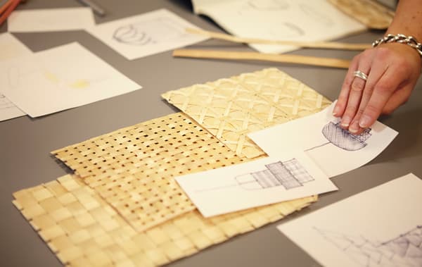 Une personne déposant des échantillons de bambou tissé et des croquis sur une table.