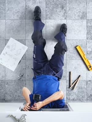Une personne en bleu de travail travaille sous un plancher, entourée d'outils et de plans de construction.
