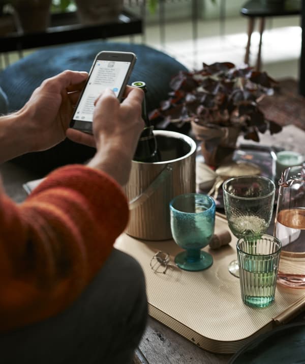 Une personne pianotant sur son téléphone devant une table basse remplie de verres.