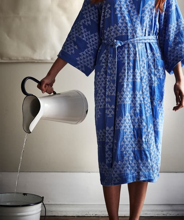 Une personne portant un kimono bleu à motif versant de l’eau qui coule d’une cruche blanche dans un seau.
