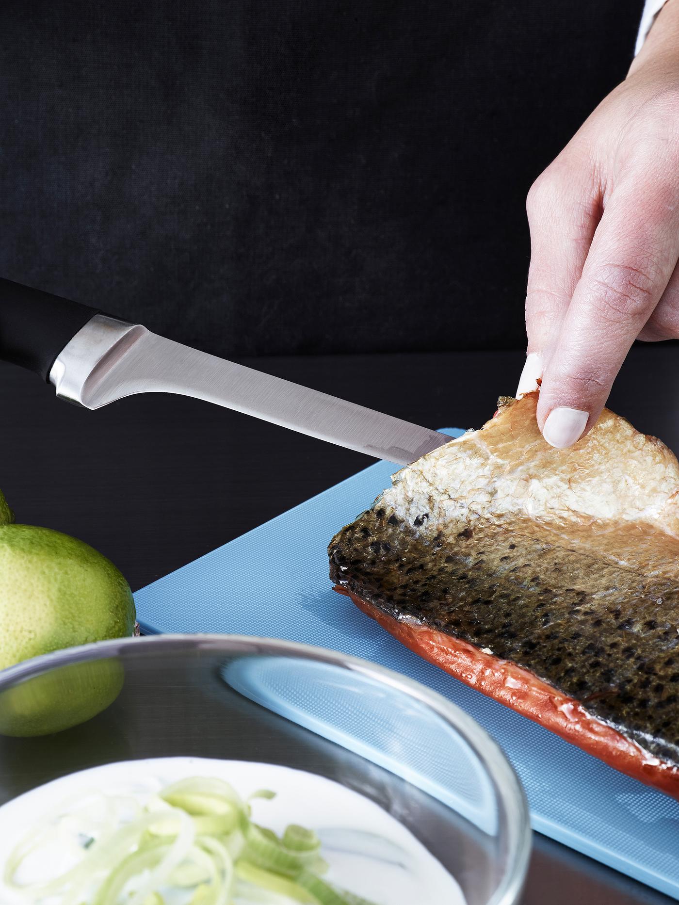 Une personne portant un tablier noir lève le filet d’un poisson à l’aide d’un couteau à filet au manche noir.