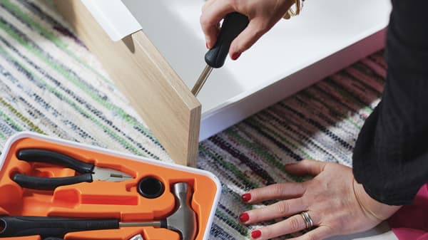 Une personne qui visse un tiroir de cuisine, avec une boîte à outil orange.