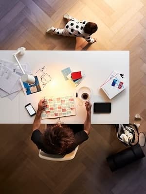Une personne travaille à un bureau tandis qu'un enfant joue par terre.
