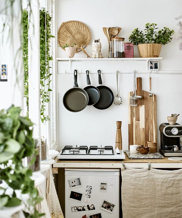 Une petite cuisine avec une table de cuisson, des ustensiles suspendus et une étagère de présentation.