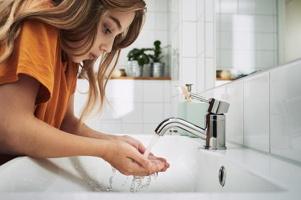 Une petite fille portant un t-shirt orange récoltant dans ses mains de l'eau du robinet.