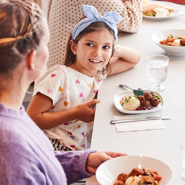 Une petite fille regarde sa mère. Un repas pour enfant est placé sur la table devant elle. 

