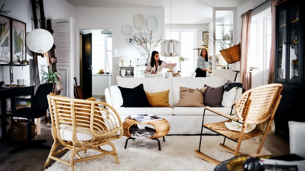 Une pièce blanche au style rustique avec deux femmes derrière un canapé BACKSÄLEN, et à l’avant un tapis et deux fauteuils.