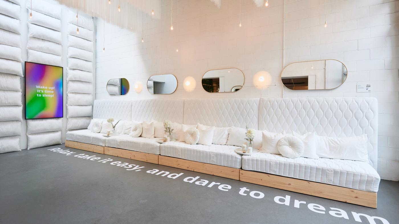 Une pièce blanche avec des matelas contre le mur en guise de canapé, des miroirs sur le dessus et des oreillers contre le mur. 