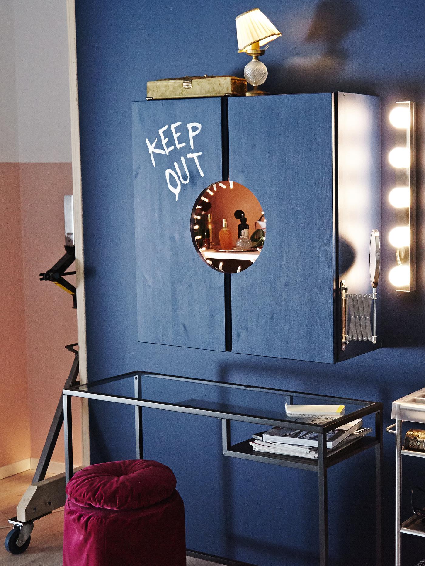 Une pièce bleue avec une coiffeuse fabriquée à partir d’une armoire peinte en bleu, d’une table pour ordinateur portable VITTSJÖ et d’un pouf bordeaux.