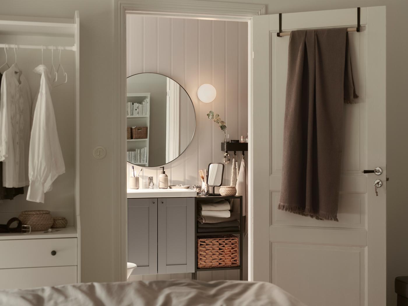 Une pièce dont la porte est ouverte, des cintres STAJLIG et une serviette de bain VALLASÅN gris clair/brun, un miroir dans la salle de bain.