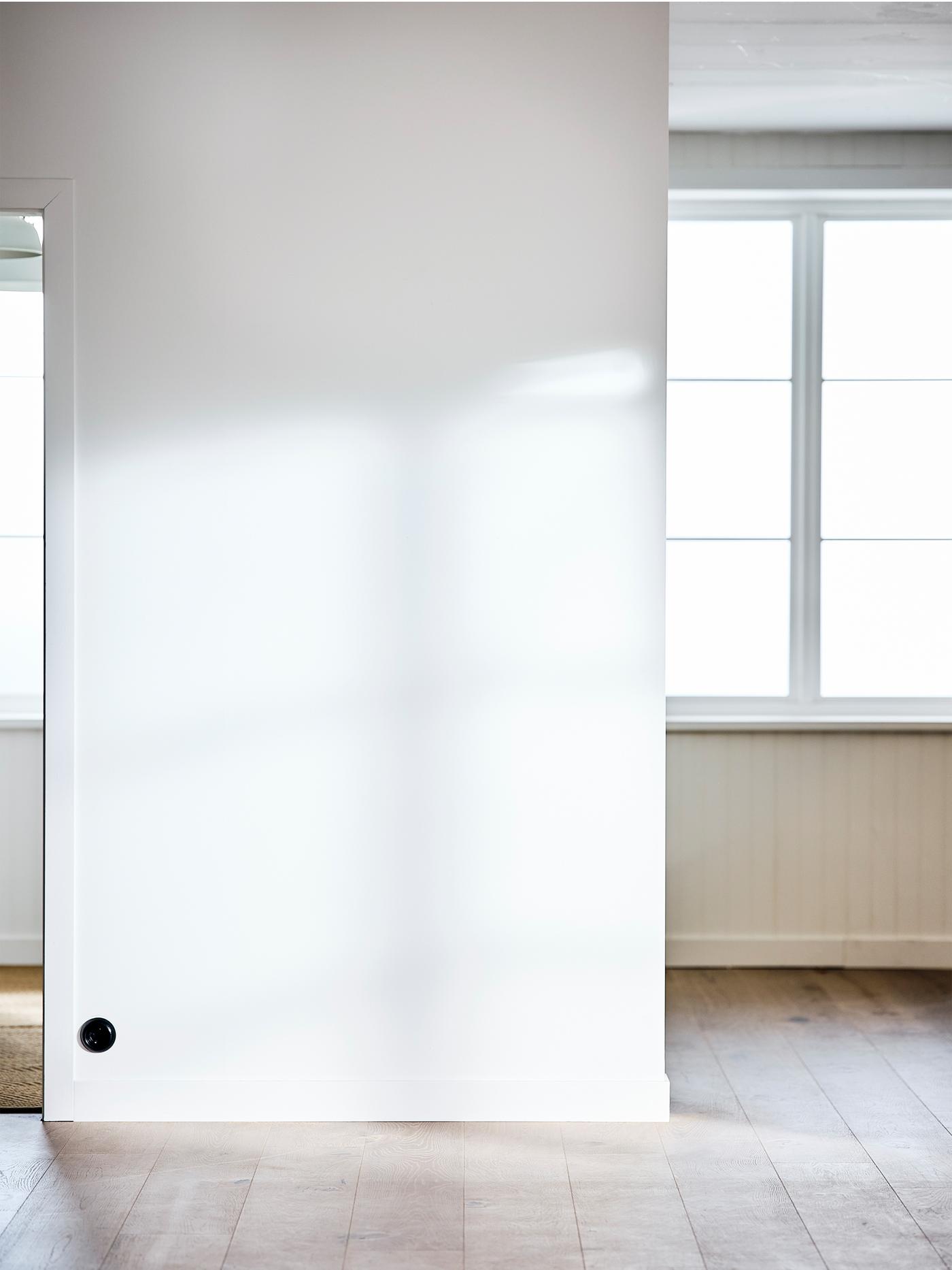 Une pièce vide avec une grande fenêtre, des murs peints en blanc et un plancher en bois blanchi.