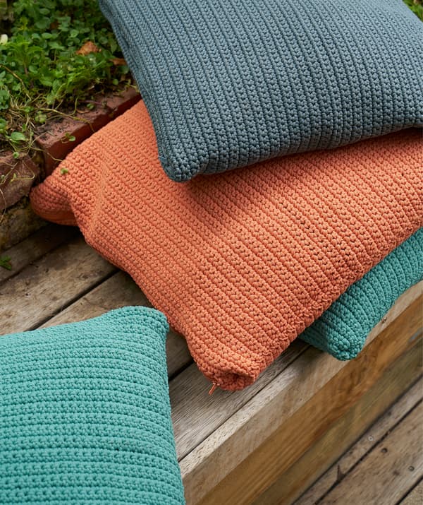 Une pile de coussins orange, bleus et turquoises sur un sol en caillebotis.