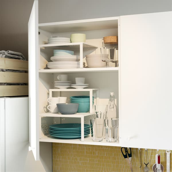 Une porte d’armoire de cuisine est ouverte et montre des demi-étagères blanches VARIERA qui organisent les assiettes, bols et autres.
