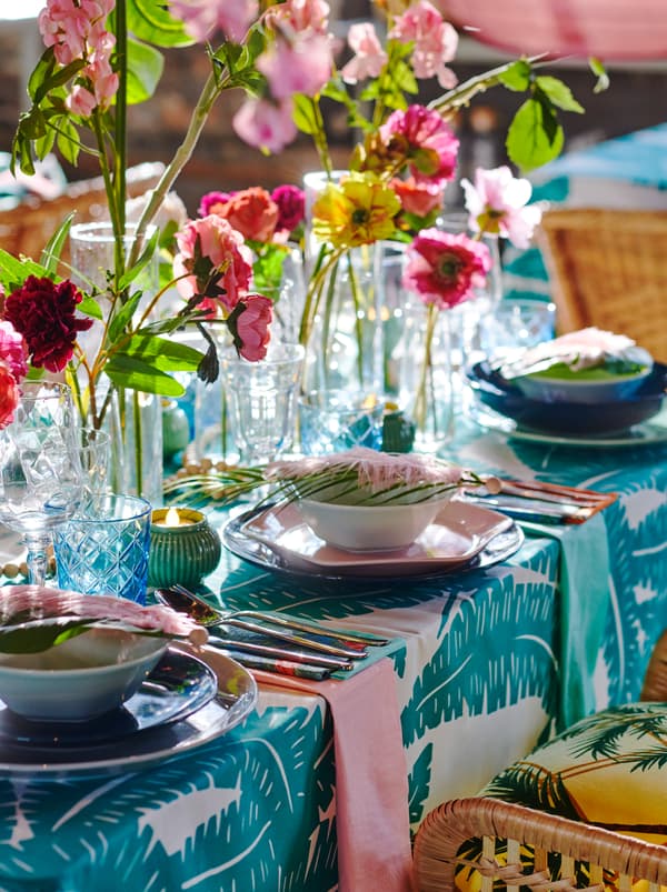 Une portion de table dressée avec des assiettes FORMIDABEL, des textiles à motifs colorés et des fleurs et feuilles artificielles.