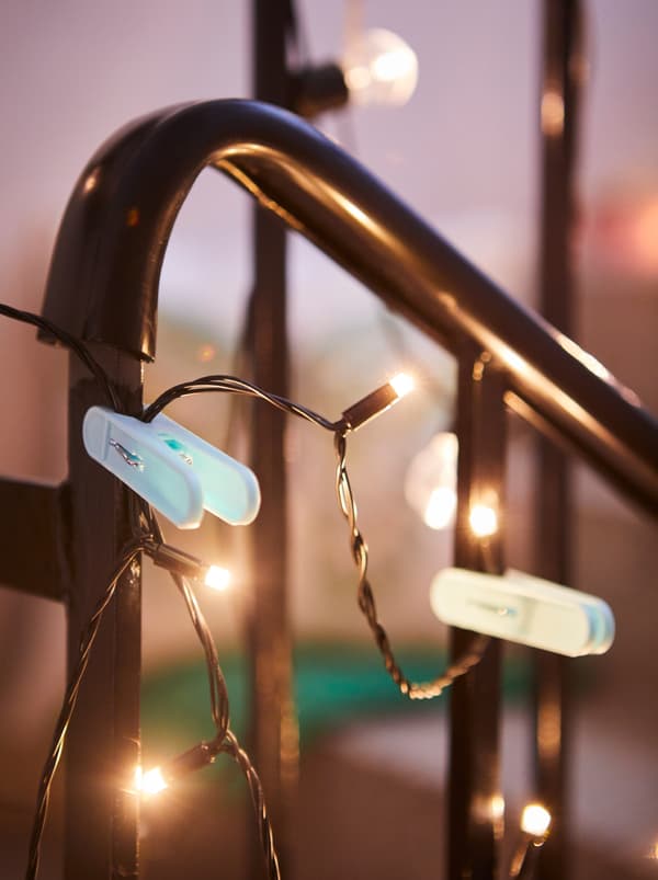 Une rampe d’escalier dans un immeuble à appartements, décorée d’une guirlande lumineuse SVARTRÅ fixée avec des pinces à linge TORKIS.