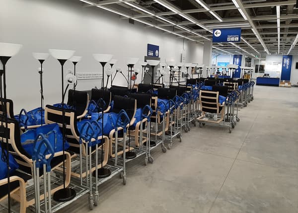 Une rangée de chariots, chacun contenant un fauteuil et un sac bleu IKEA FRAKTA.