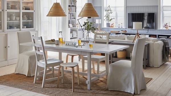 Une salle à manger spacieuse et lumineuse. La table est déployée et des tabourets servent de sièges d’appoint.