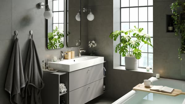 Une salle de bain calme et apaisante avec une baignoire moderne et élégante, un large lavabo double avec rangement, 2 miroirs et des plantes d’intérieur.