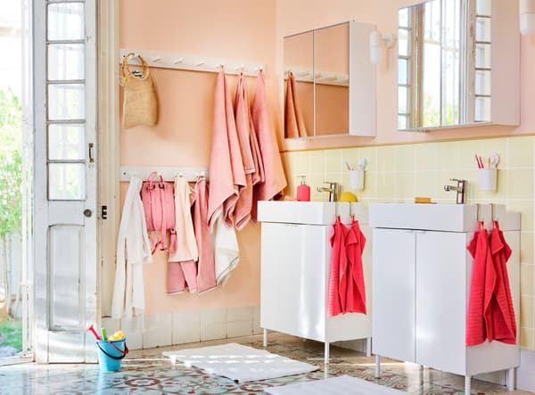 Une salle de bain lumineuse avec des serviettes en rose et corail, et des sacs au mur.