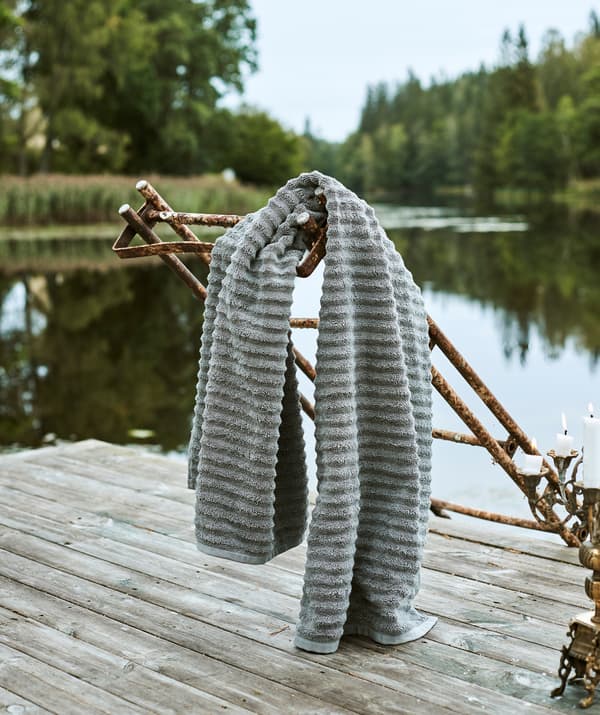 Une serviette grise toute douce est suspendue à une échelle rouillée qui mène d’un ponton à un lac.