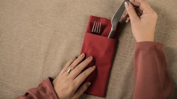 Une simple pochette faite d'une serviette de table est remplie par quelqu'un avec des couverts. 