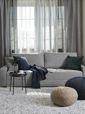 Une table basse noire se trouve devant un canapé-lit 2 places GRÄLVIKEN dans un salon aux couleurs terreuses. 