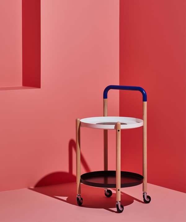 Une table d'appoint sur roulettes avec un cadre en bois et un plateau inférieur, dans une pièce rose.