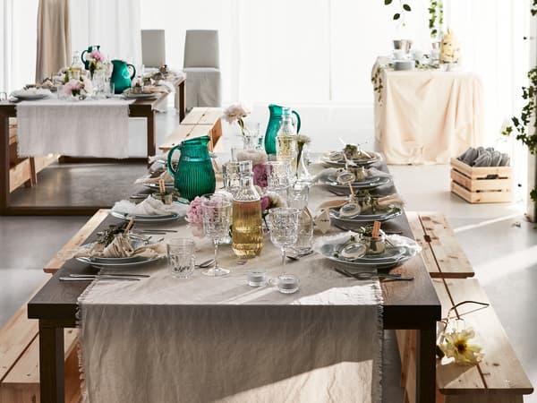 Une table de fête dressée pour une occasion spéciale au milieu d’un espace blanc ouvert avec d’autres tables en arrière-plan et un décor verdoyant.