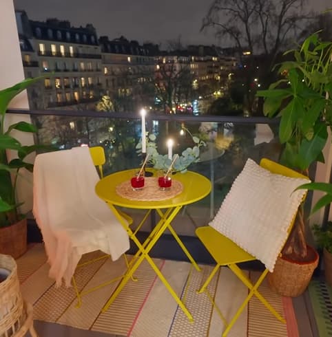 Une table d'extérieur jaune ronde avec deux chaises et des verres posés, sur un balcon.