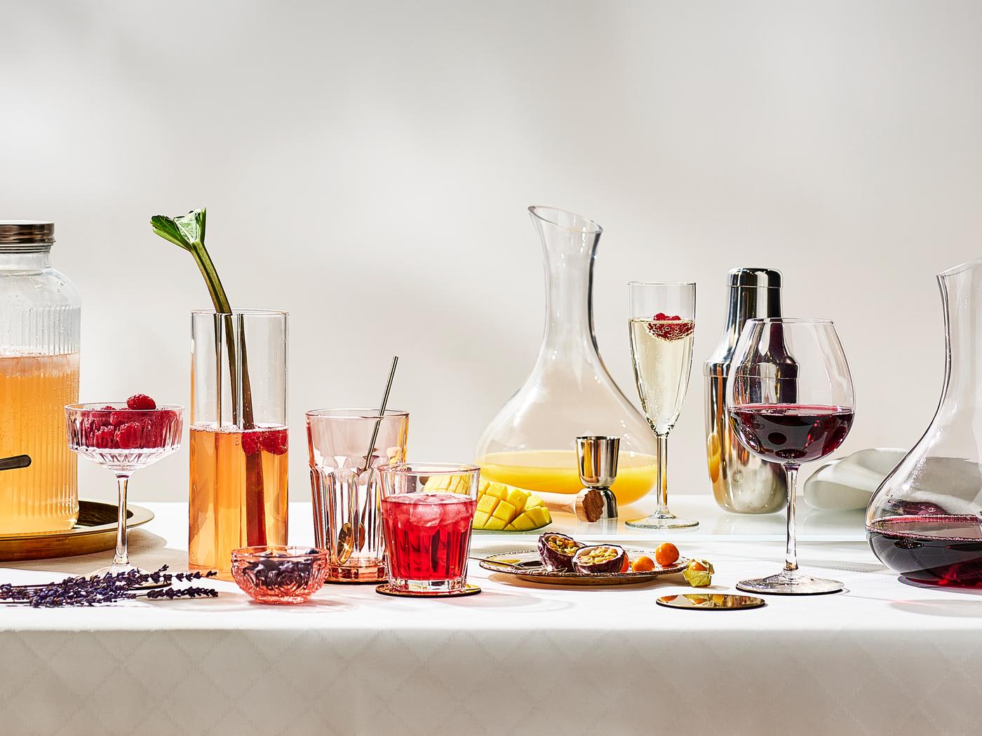 Une table festive avec des fruits et différents verres remplis de plusieurs boissons sur une nappe blanche.