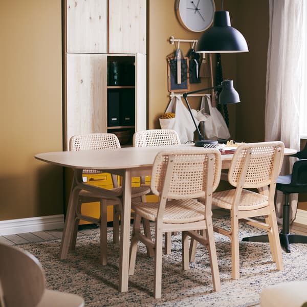 Une table VOXLÖV avec 4 chaises, sur un tapis tissé à plat MELHOLT, une horloge murale ROTBLÖTA accrochée au mur et une lampe suspendue.