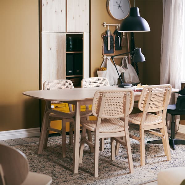 Une table VOXLÖV avec 4 chaises, sur un tapis tissé à plat MELHOLT, une horloge murale ROTBLÖTA accrochée au mur et une lampe suspendue.