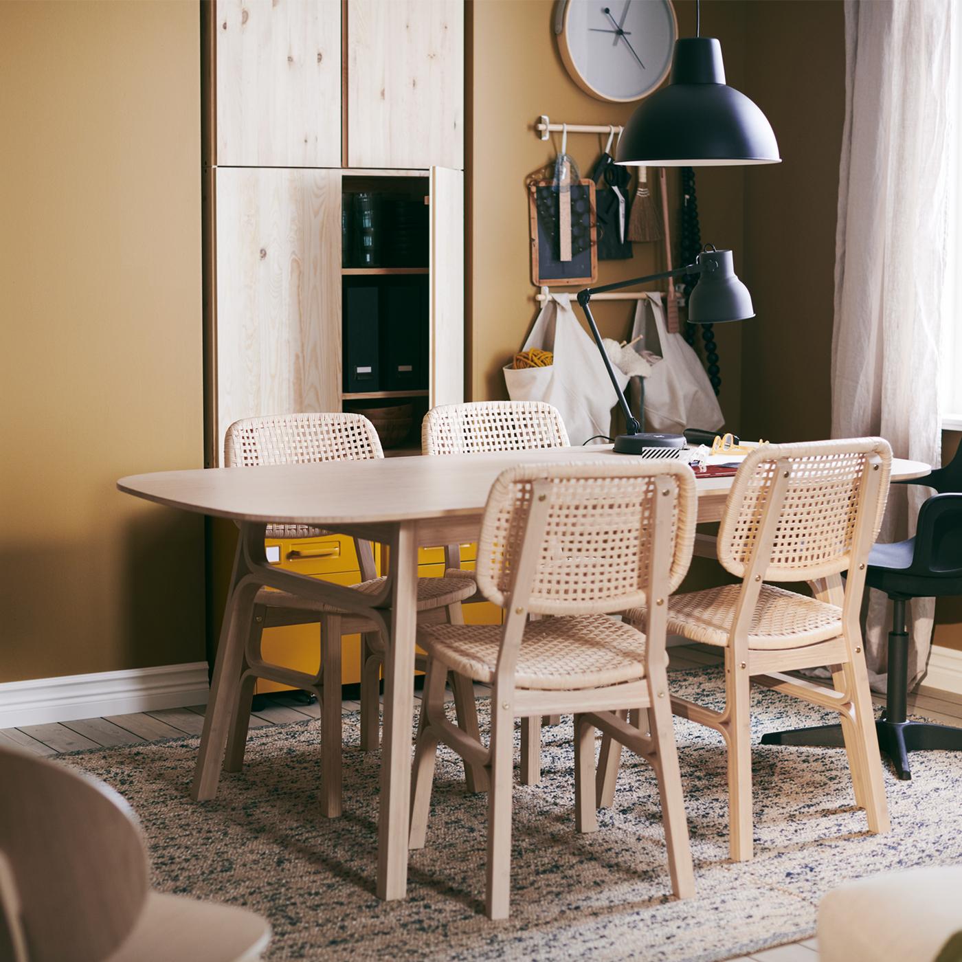 Une table VOXLÖV avec quatre chaises, sur un tapis tissé plat MELHOLT, une horloge murale ROTBLÖTA et une suspension.