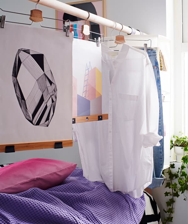 Une tête de lit composée d'une tige surélevée sur laquelle sont suspendus des vêtements et des œuvres d'art fait office de paravent.