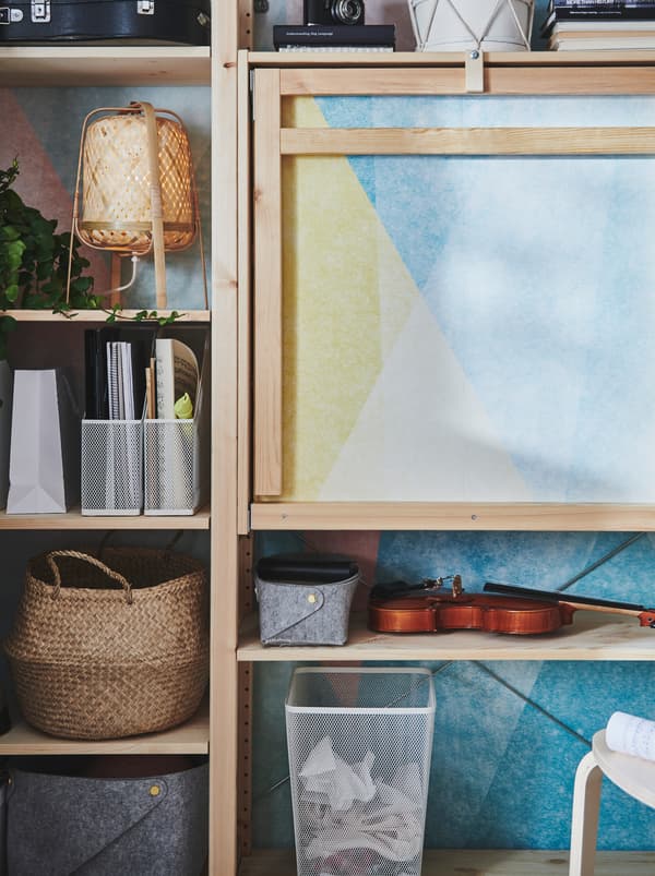 Une unité de rangement IVAR en bois dotée d’une table pliable en bois non peint, avec des objets en métal, rotin et feutre sur les étagères.