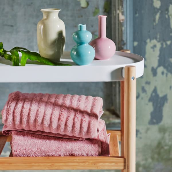 Une variété de vases colorés placés sur une table d’appoint en blanc et bois. Des serviettes rose clair sont placées sur la tablette en bois.