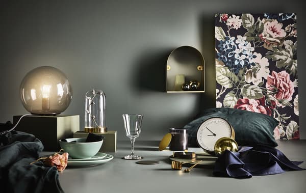Une variété d'objets disposés sur une surface sur un fond sombre, notamment une horloge, une lampe de table et une cloche de verre.
