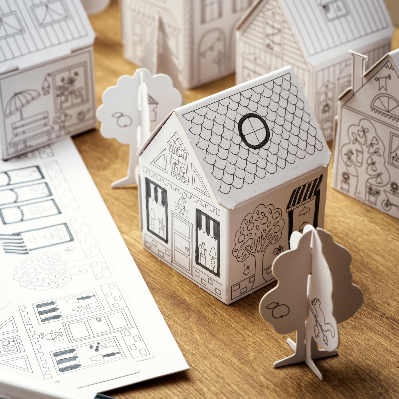 Une ville en carton MÅLA pour enfants avec des maisons et des arbres sur une surface en bois.