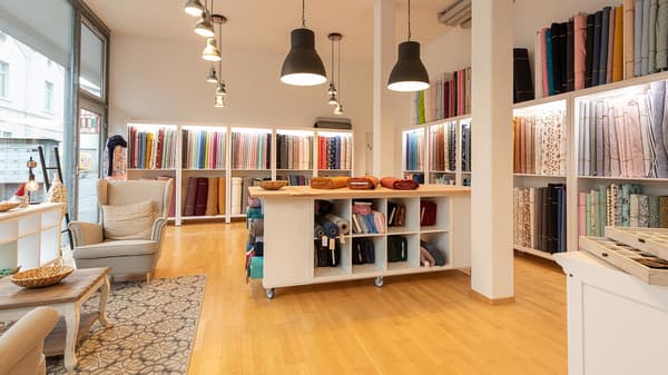 Une vue intérieure d'un magasin de tissus avec des étagères remplies de balles de tissu, un coin salon avec des fauteuils et une grande table de coupe.